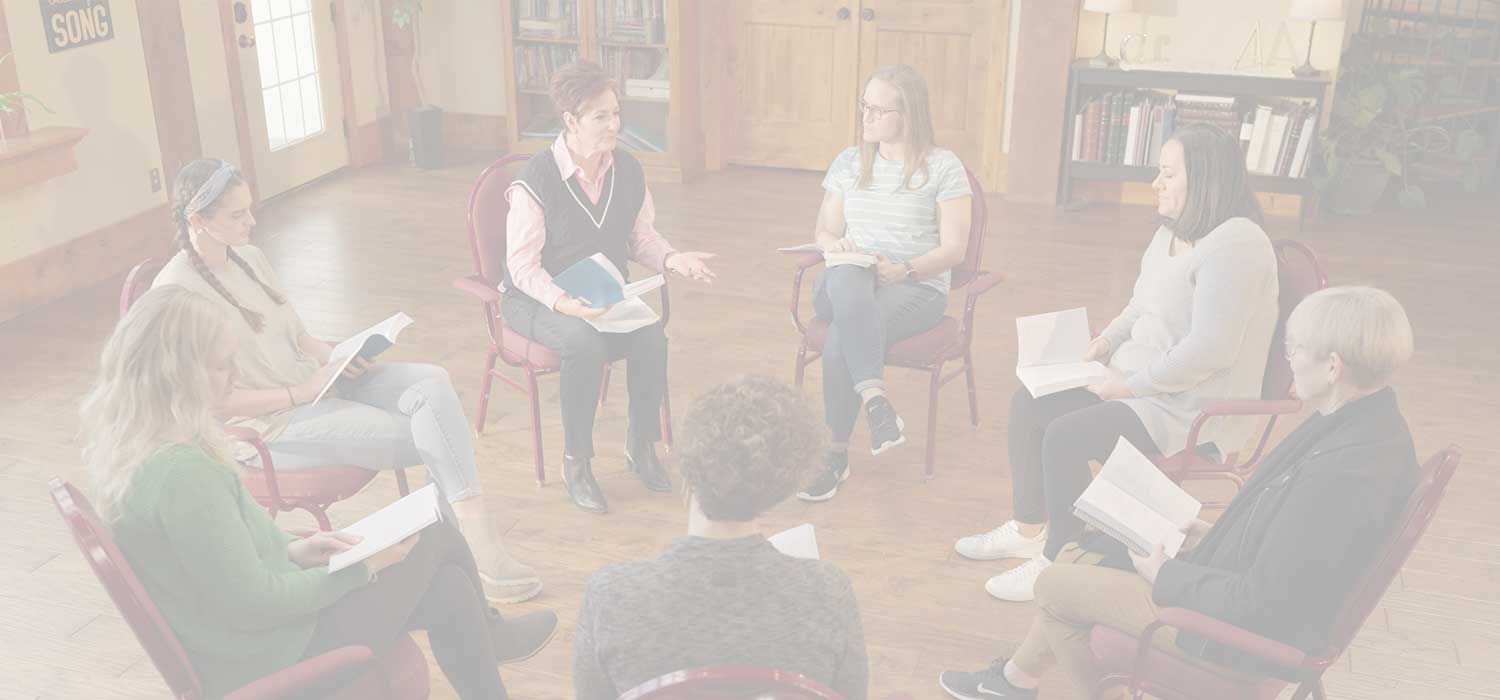 Women seated in a circle at a SAL 12-Step meeting, reading together from recovery materials.